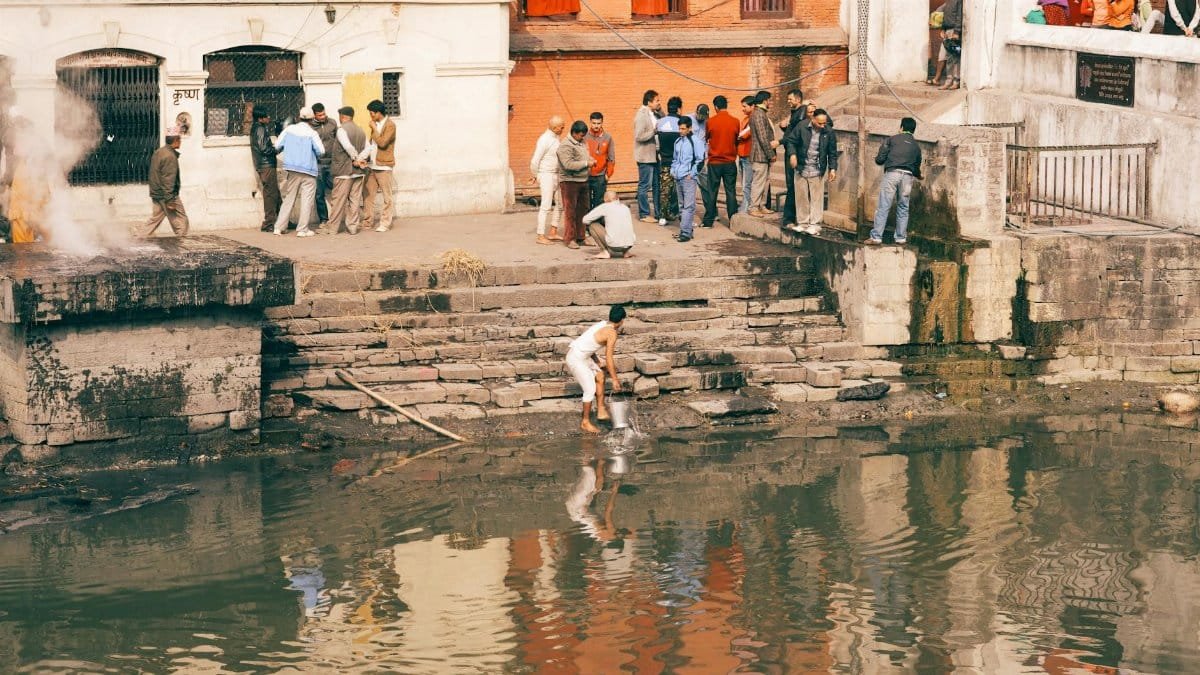 A group gathers for a traditional ritual at a riverfront ghat, highlighting cultural practices.