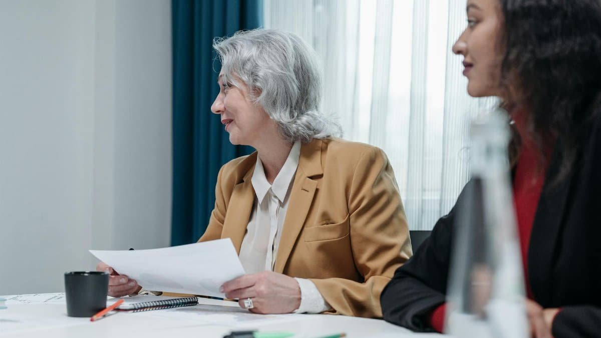 Two businesswomen engaged in a meeting discussing documents at an office desk.