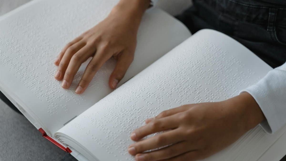 Close-up of hands reading a braille book, emphasizing accessibility and education.