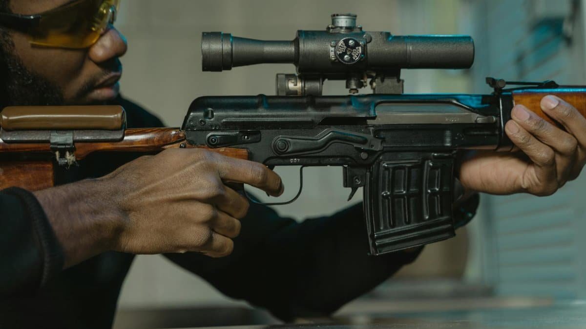 Close-up of a man handling a rifle at an indoor shooting range, wearing safety glasses.