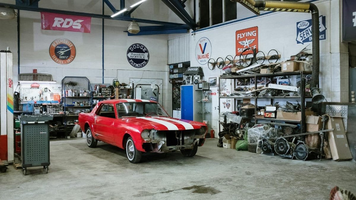 A vintage red car undergoing restoration in a well-equipped workshop with various tools and auto parts.