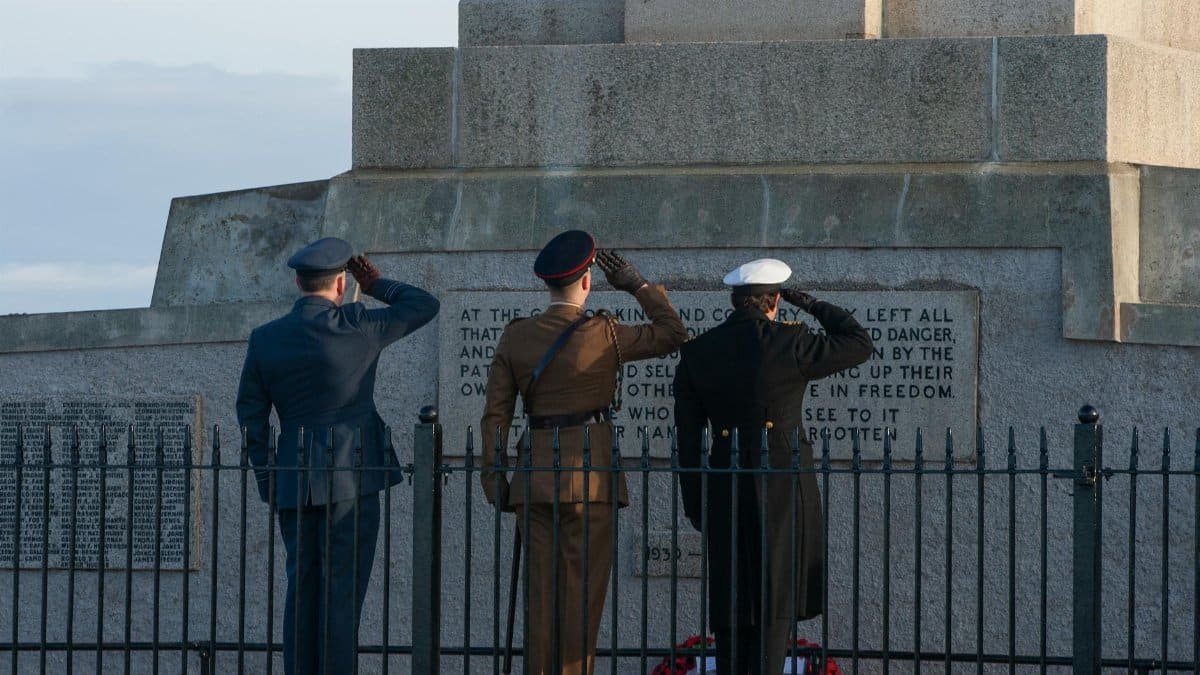 Three soldiers in uniform salute a World War I memorial, honoring fallen comrades.