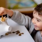 Young boy smiling while saving money in a crowned piggy bank, demonstrating financial responsibility.