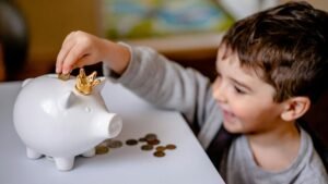 Young boy smiling while saving money in a crowned piggy bank, demonstrating financial responsibility.