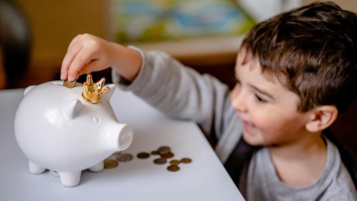 Young boy smiling while saving money in a crowned piggy bank, demonstrating financial responsibility.