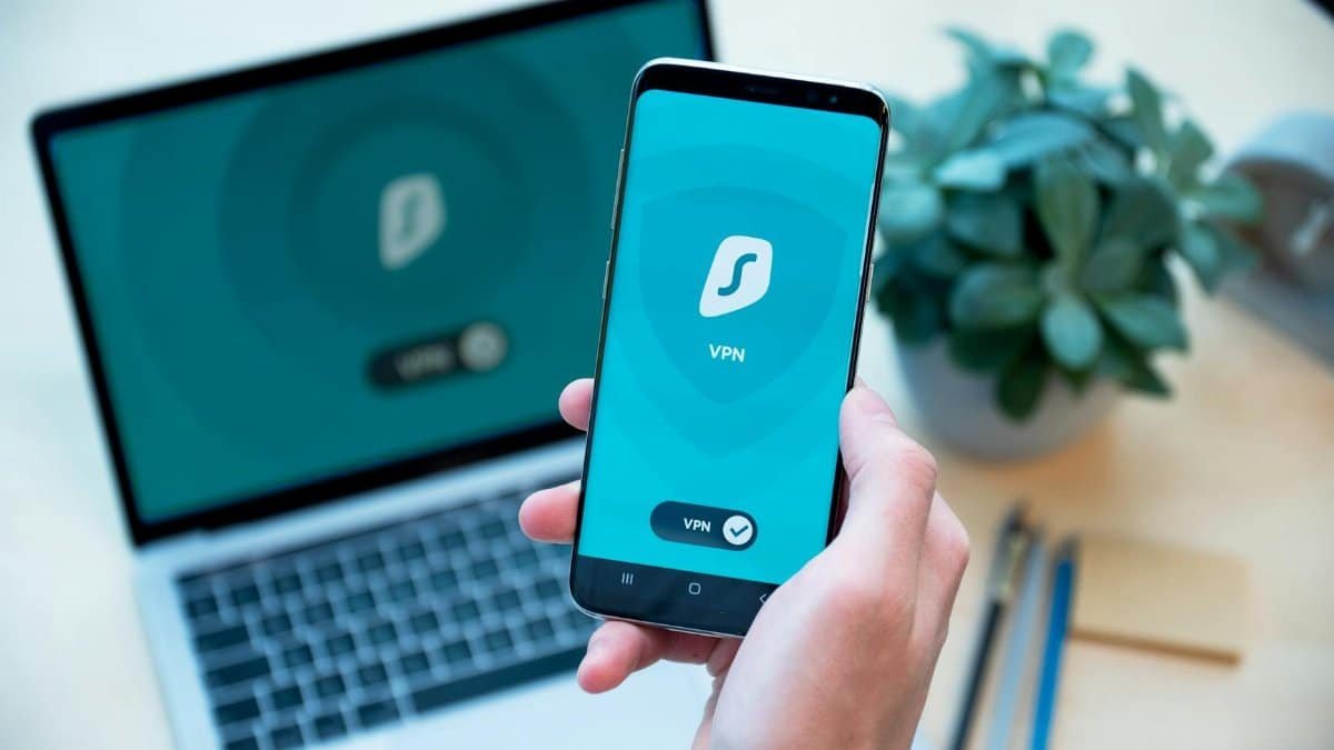 Close-up of a hand holding a smartphone with VPN app, laptop in the background, showcasing digital security.