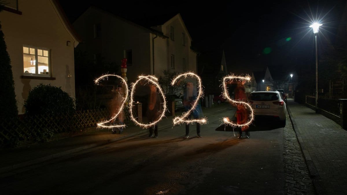Sparkler light painting forming '2025' in a festive night street scene.