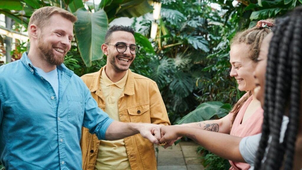 A diverse team of adults enjoying a fist bump gesture in an indoor greenhouse setting.