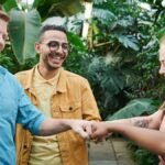 A diverse team of adults enjoying a fist bump gesture in an indoor greenhouse setting.