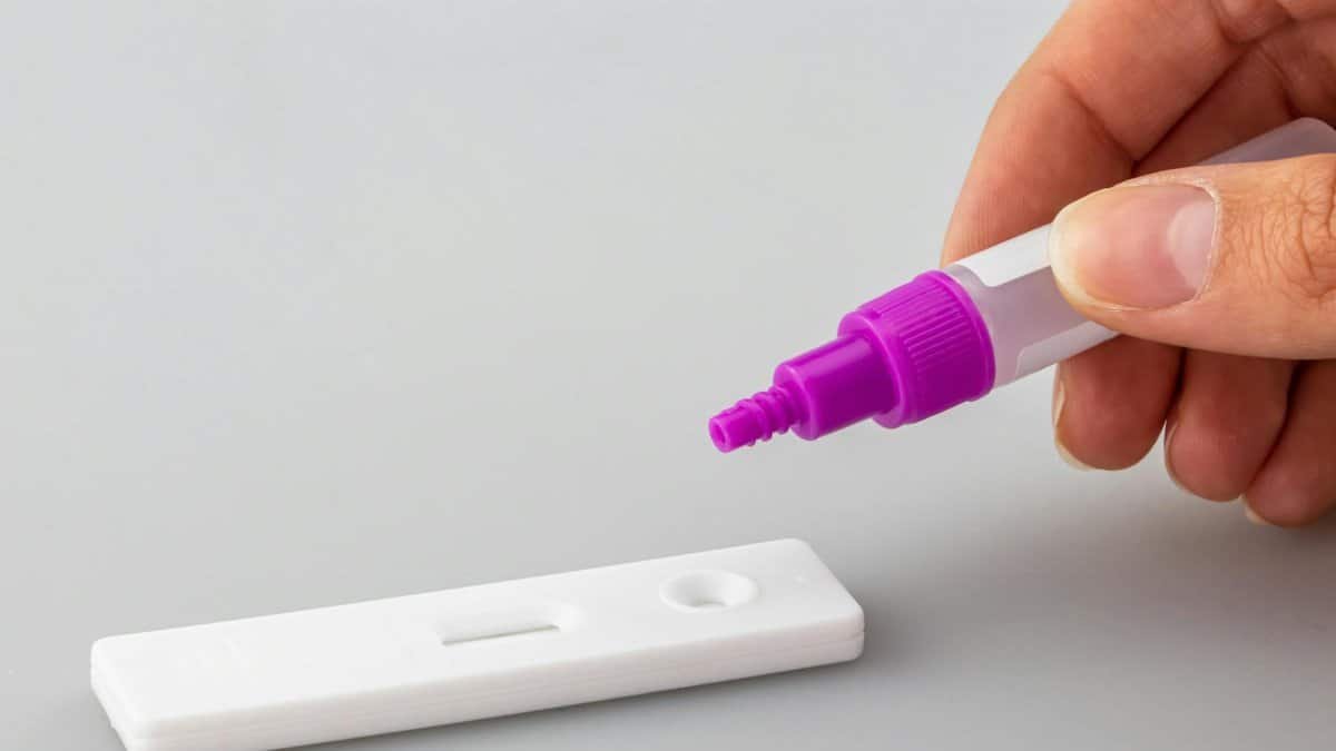 Close-up of a hand applying liquid on a rapid test kit, against a white surface.