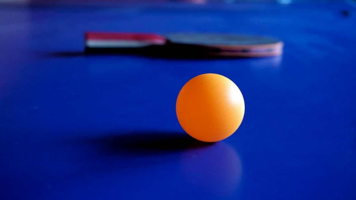 Vibrant orange ping pong ball with a table tennis racket on a blue table, emphasizing sport and leisure.