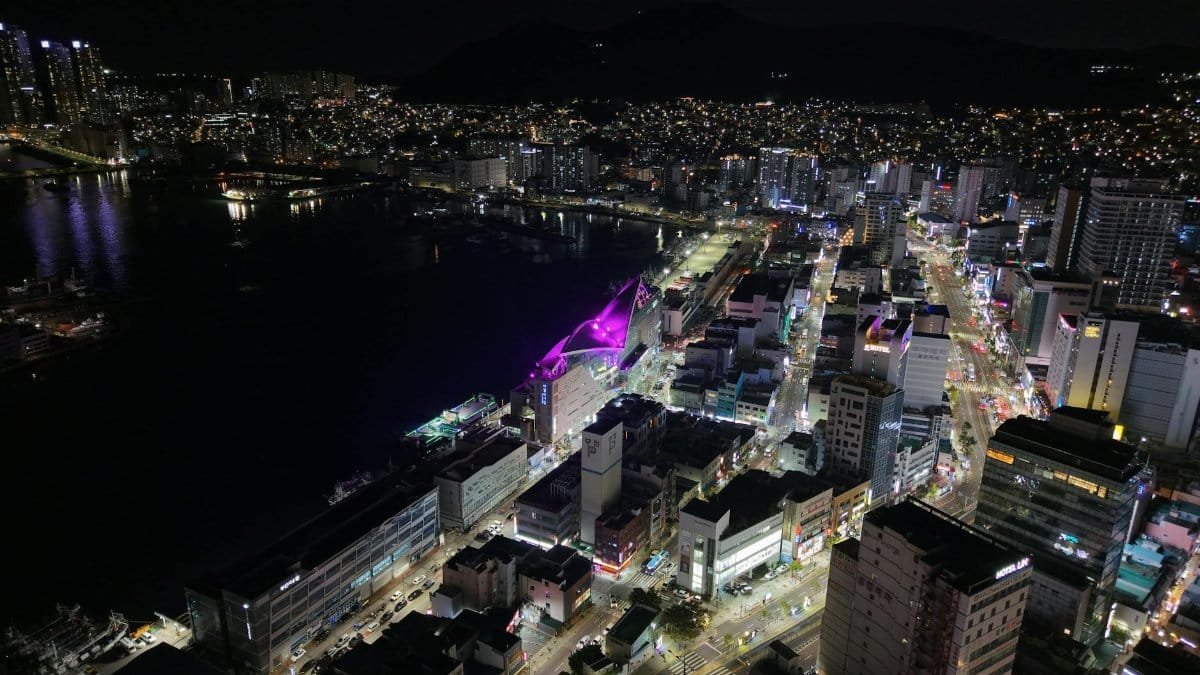 A stunning aerial shot capturing the vibrant city lights of Busan at night, showcasing urban architecture.