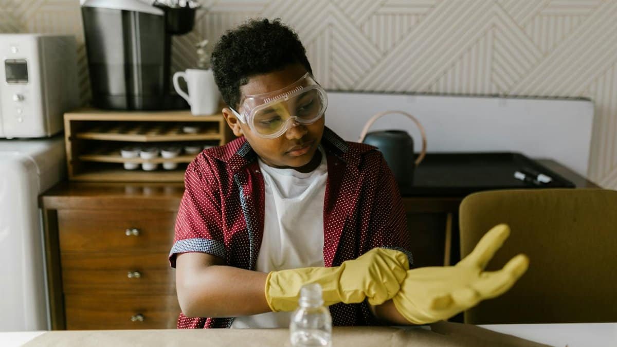 Young boy wearing goggles and gloves preparing for a science experiment indoors.