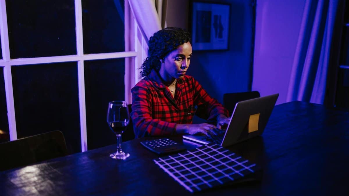 A woman working on a laptop at night, illuminated by blue light, showcasing remote work lifestyle.