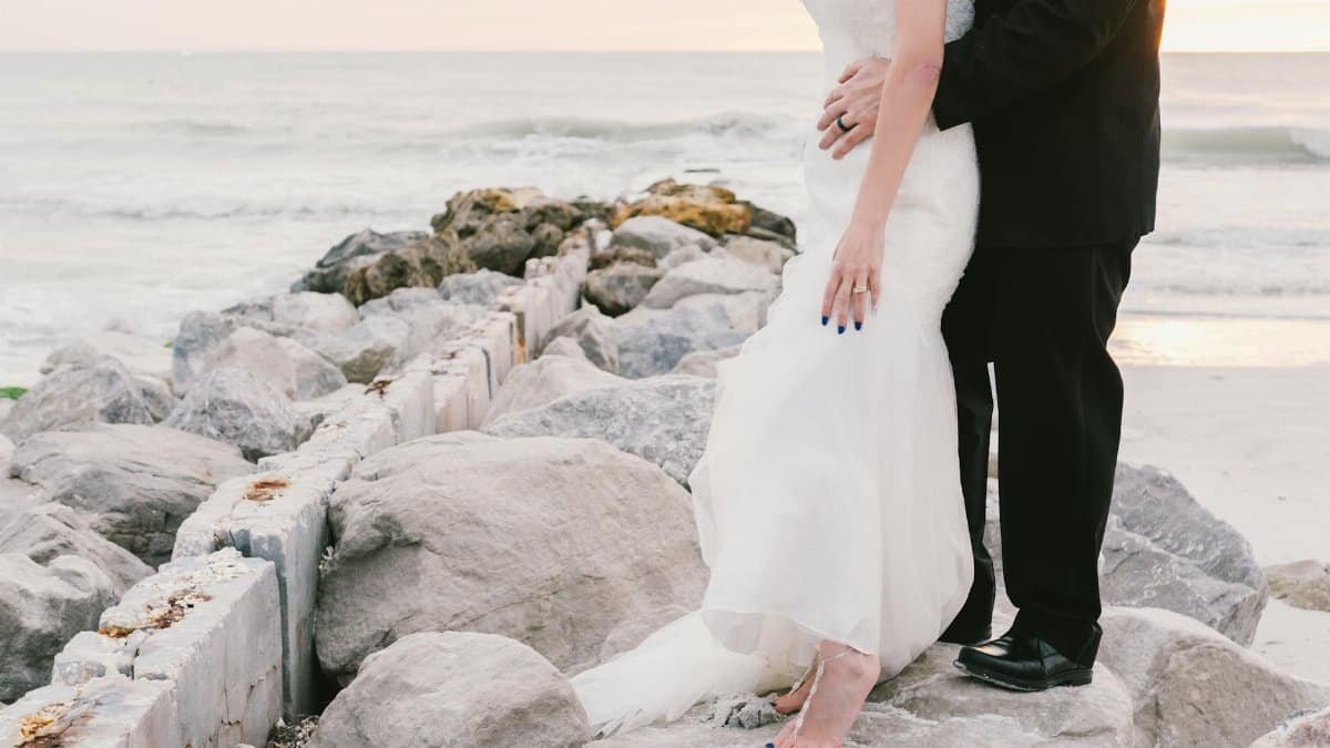 A barefoot couple stands on beach rocks during sunset, capturing a romantic wedding moment in St. Petersburg.