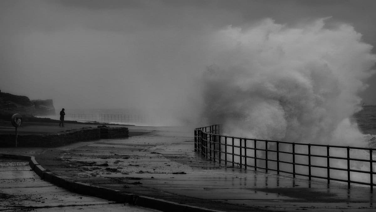 A powerful wave crashes against a stormy shore, creating a dramatic and moody scene.