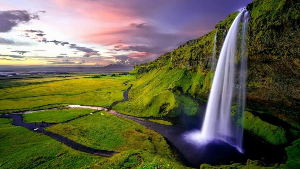 Stunning waterfall cascading over green cliffs during a vibrant Icelandic sunset.