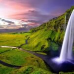 Stunning waterfall cascading over green cliffs during a vibrant Icelandic sunset.