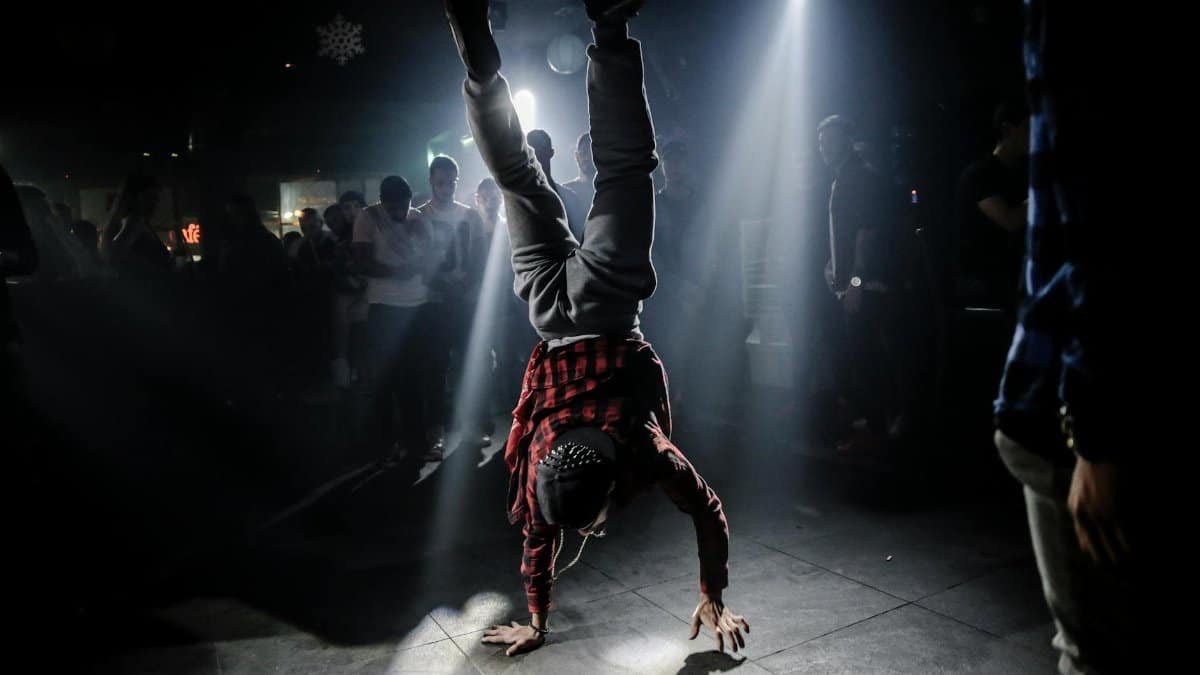 Breakdancer in plaid shirt performs a handstand in a lively club setting.