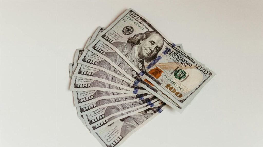 Crisp US hundred dollar bills fanned out on a clean white surface, representing wealth and finance.