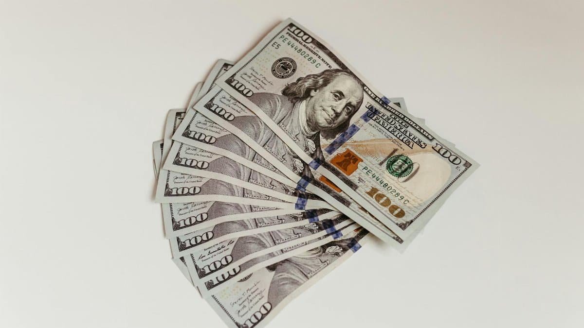 Crisp US hundred dollar bills fanned out on a clean white surface, representing wealth and finance.