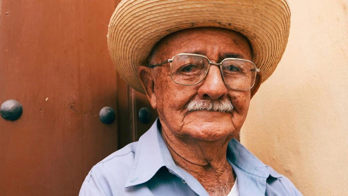 Close-up portrait of a senior man wearing glasses and a straw hat, showcasing wisdom and character.