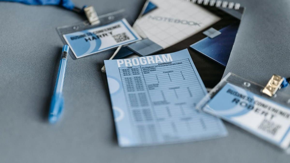 Close-up of conference materials including name tags, program, and pen on a gray surface.
