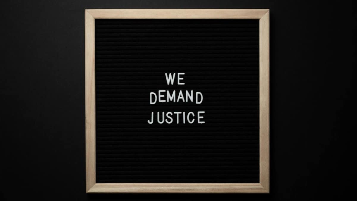 Sleek protest sign with 'We Demand Justice' text on black felt board. Minimalist design.