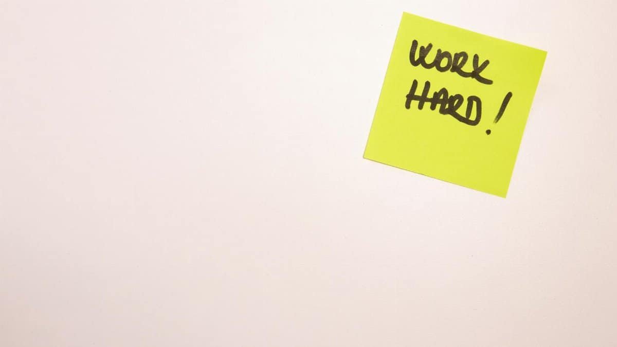 Bright yellow sticky note on white background with 'Work Hard' written, ideal for motivational content.