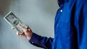 A person in a blue shirt holding a stack of US dollar bills, symbolizing wealth and finance.