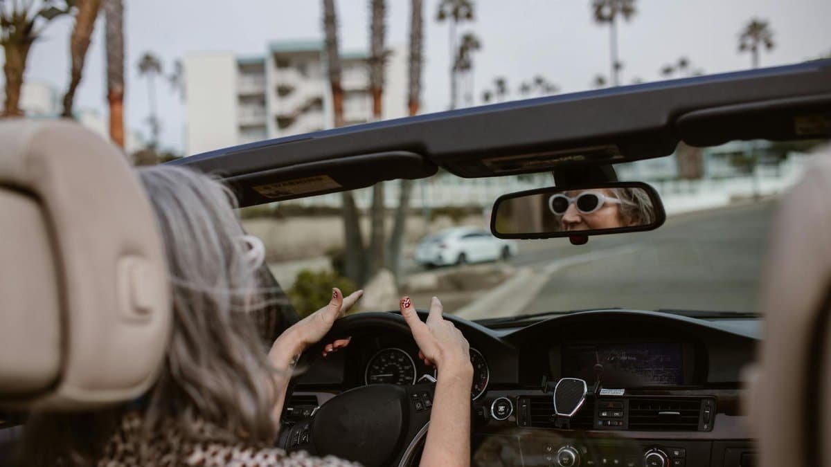 Senior woman enjoying a drive in a convertible with palm trees lining the road.