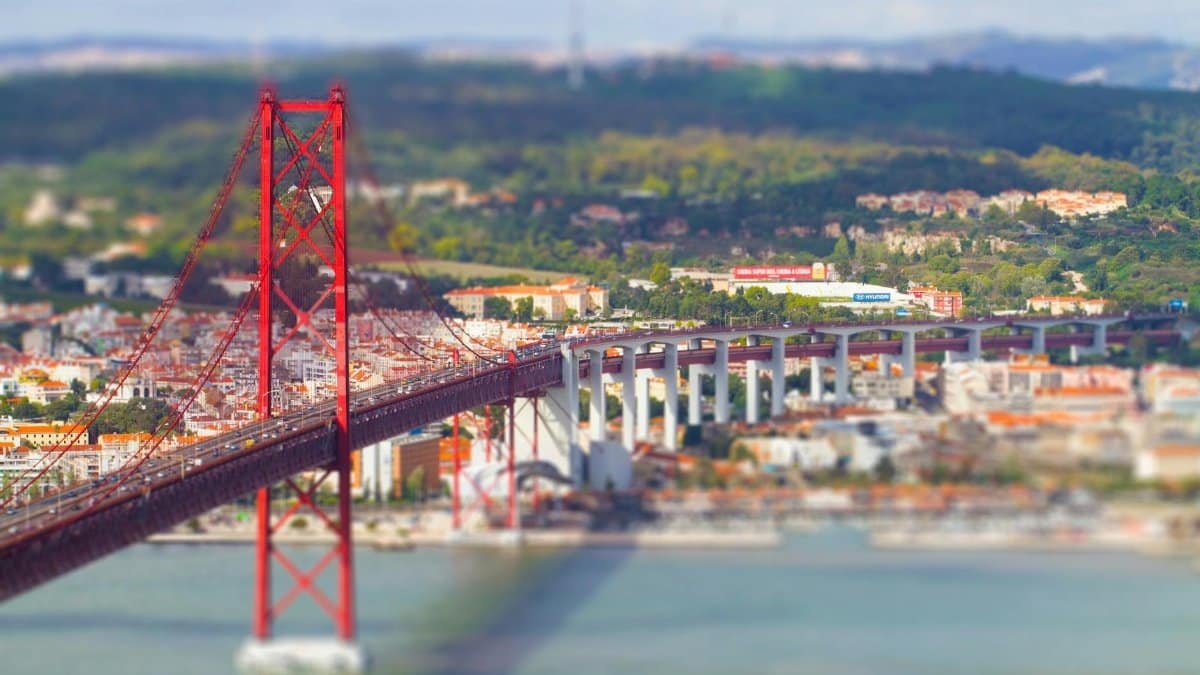 A vibrant tilt-shift view of Lisbon's 25 de Abril Bridge spanning the Tagus River.