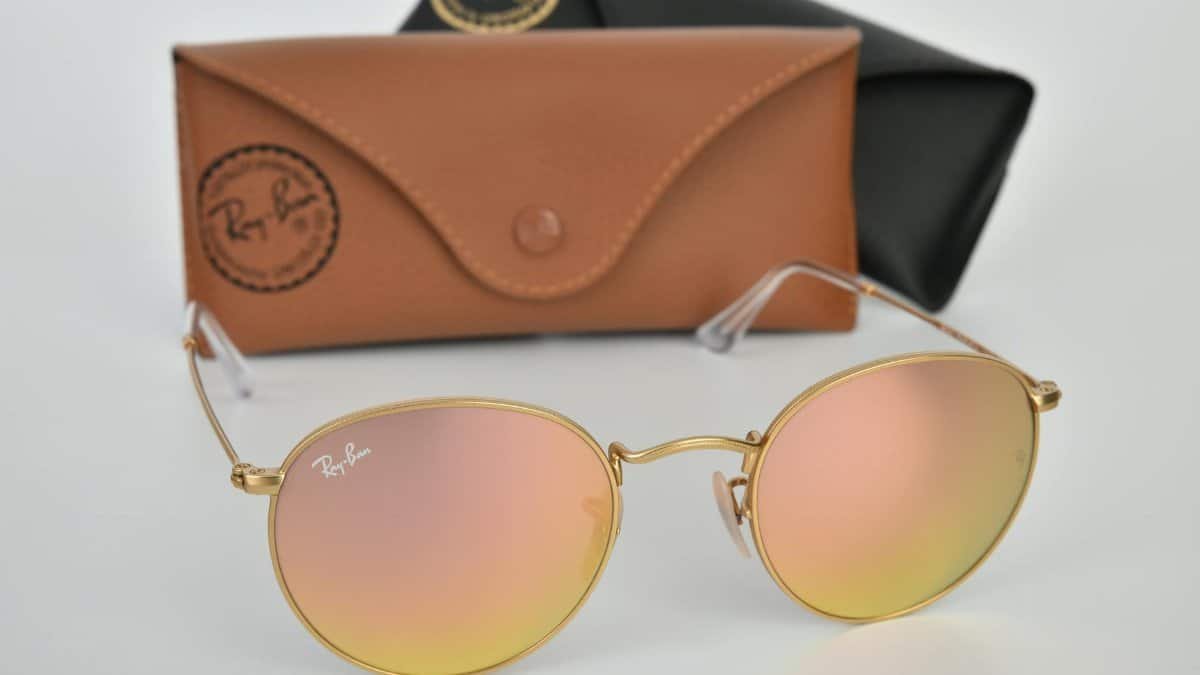 Trendy Ray-Ban round sunglasses with gold frames and reflective lenses. Includes branded case on a white backdrop.