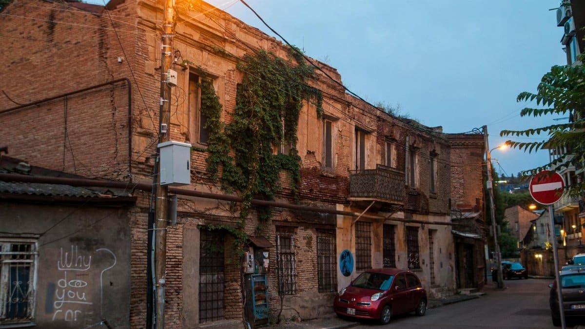 A rustic street in Tbilisi with old brick buildings and a vintage car at twilight.