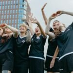 A joyful moment with women soccer players celebrating victory on an outdoor field with a building backdrop.