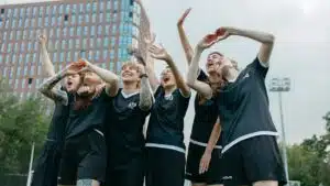 A joyful moment with women soccer players celebrating victory on an outdoor field with a building backdrop.