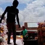 Silhouette of workers stacking large sacks at an outdoor market under a bright sky.