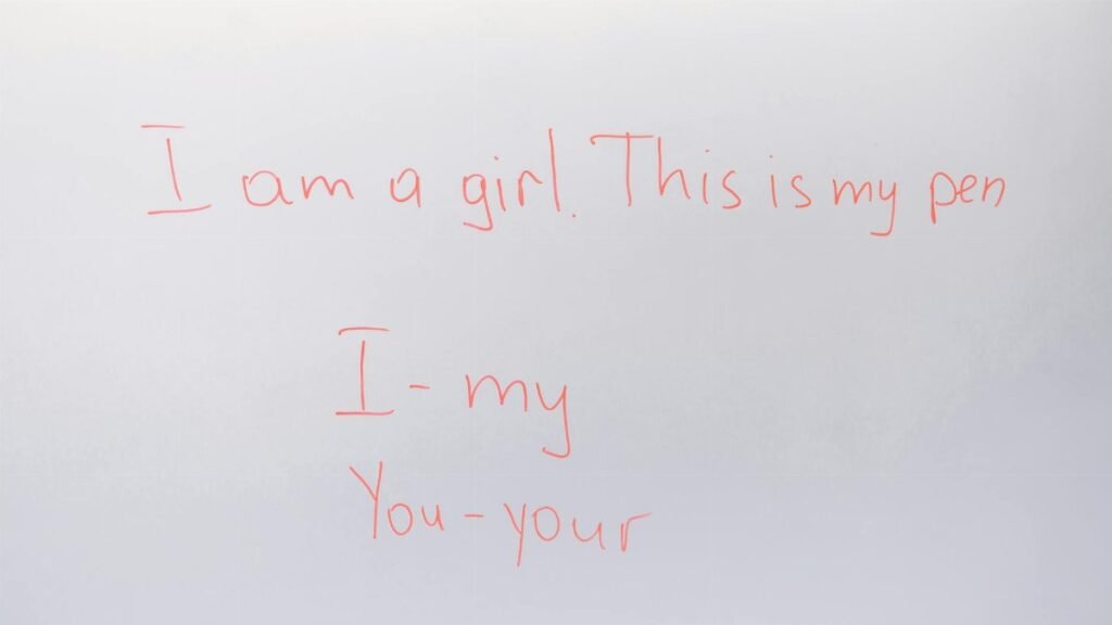 Handwritten English lesson on whiteboard with sentences and pronouns.