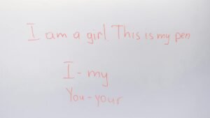 Handwritten English lesson on whiteboard with sentences and pronouns.