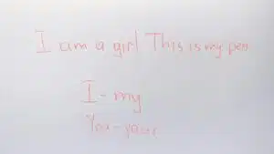 Handwritten English lesson on whiteboard with sentences and pronouns.