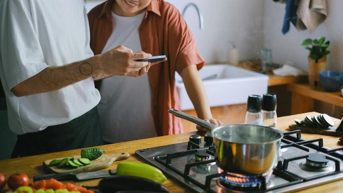 A couple cooking together and using a smartphone for recipes in a cozy kitchen.