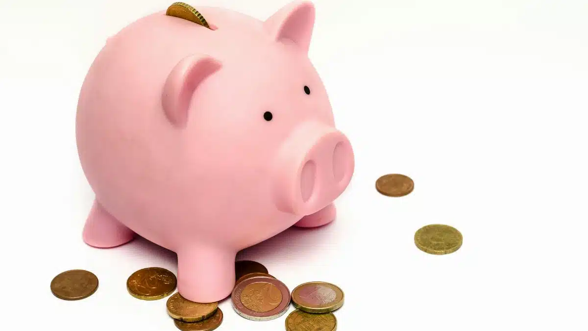 A pink piggy bank surrounded by scattered coins, symbolizing savings and financial investment.