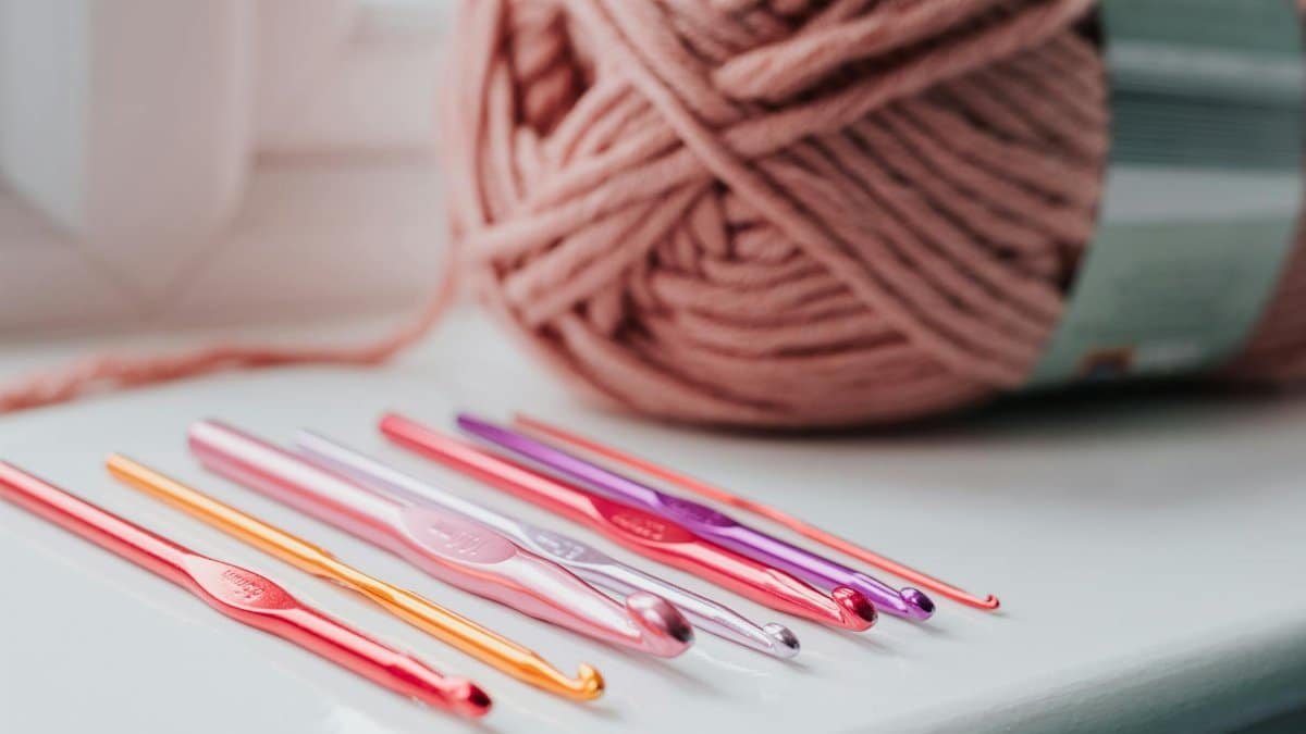 Closeup of row of multicolored crochet needles and ball of beige threads for knitting in bright room