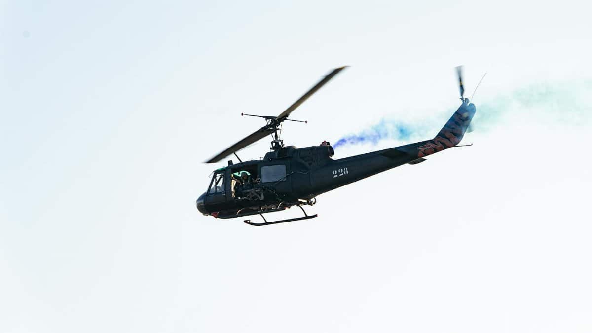 Black military helicopter performing air show with smoke trails in El Salvador.