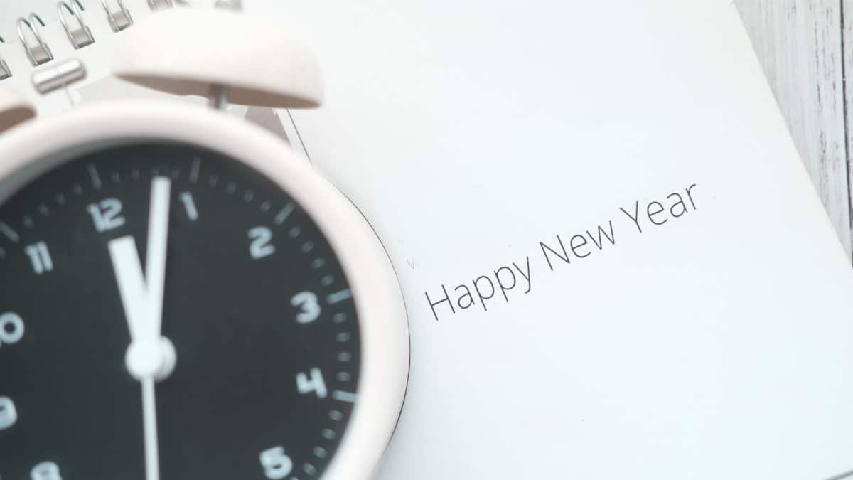 A close-up of an analog alarm clock and a 'Happy New Year' note, symbolizing the countdown to the new year.