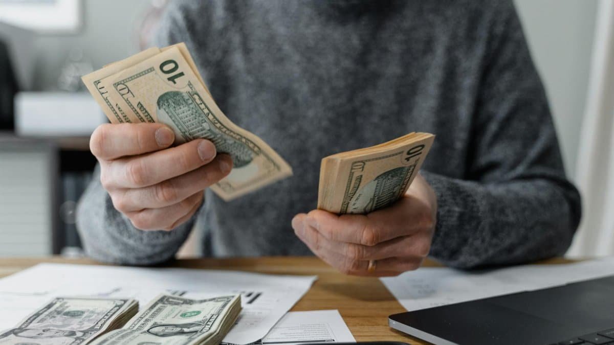 Close-up of person counting cash with a calculator and paperwork on a desk.