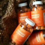 Four bottles of turmeric and ginger gummies set against a textured brown fabric backdrop.