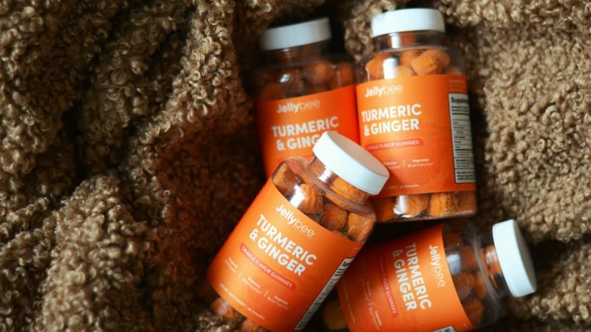 Four bottles of turmeric and ginger gummies set against a textured brown fabric backdrop.