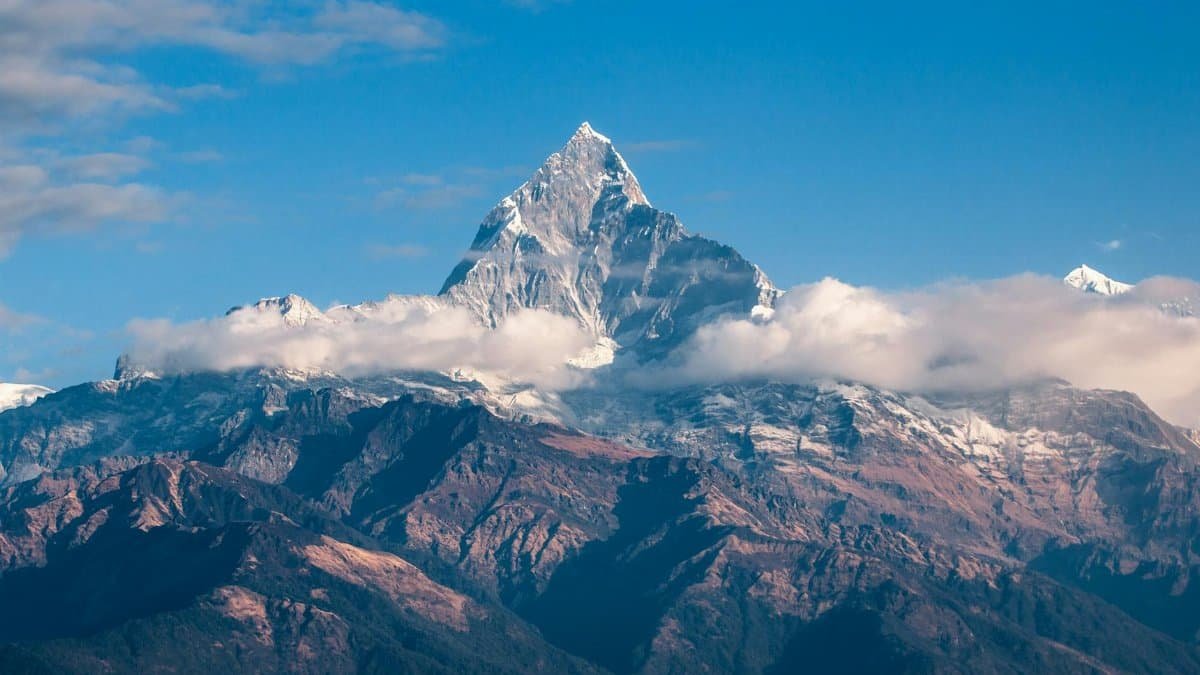 Breathtaking view of a snow-covered mountain peak surrounded by clouds during sunrise.