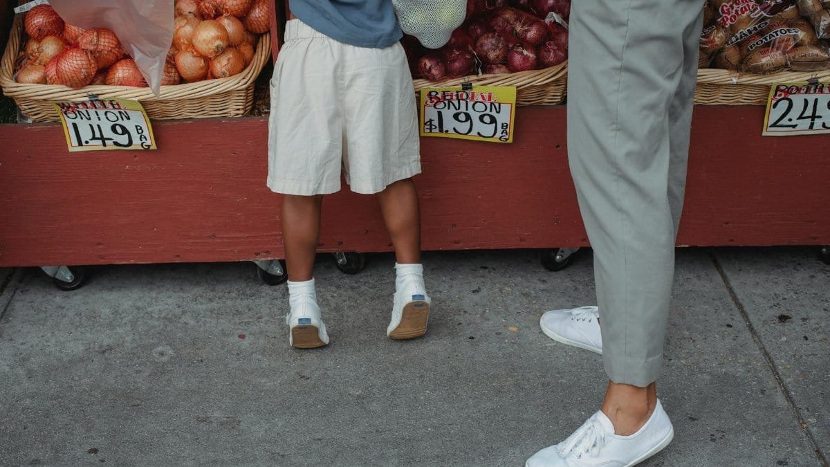 A child and adult picking fresh onions at a local farmers market outdoor stand.